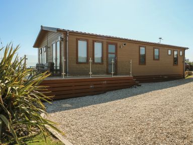 A wooden lodge with windows and decking in an outdoor area at Sunstone Lodge (Garreg Haul Lodge) Cilan near Abersoch