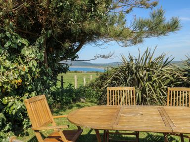 An outdoor dining area with a table and chairs overlooking the sea at Sunstone Lodge (Garreg Haul Lodge) Cilan near Abersoch
