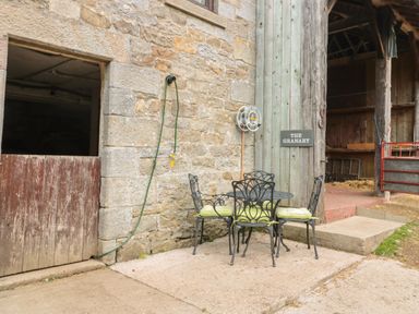 Metal table and chairs with cushions outside a stone and wooden building with a sign saying The Granary in Rothbury