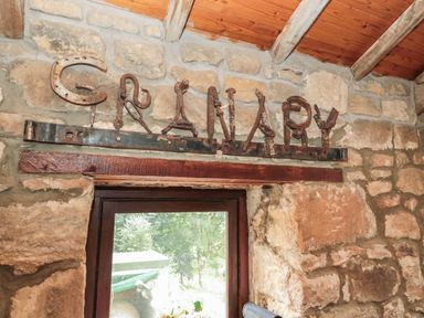A stone wall with a wooden beam above a window and metal letters spelling granary at The Granary in Rothbury