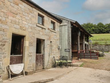 An outdoor patio with metal chairs and table beside a stone building and wooden barn doors at The Granary in Rothbury