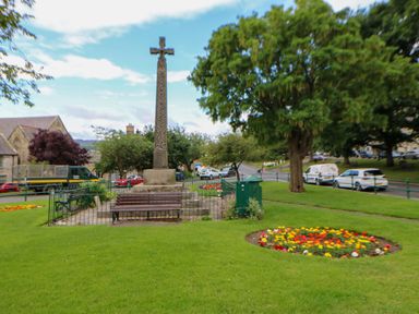A memorial with a cross and flowers surrounded by grass at The Granary in Rothbury