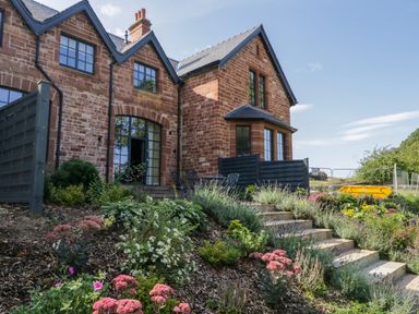 A brick house with black window frames and a garden with flowers and stairs at Tarn End Cottages 5 Talkin near Brampton Cumbria