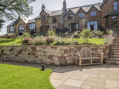 A stone terrace with a wooden bench and steps leading up to a large stone house with gardens at Tarn End Cottages 5 Talkin near Brampton Cumbria