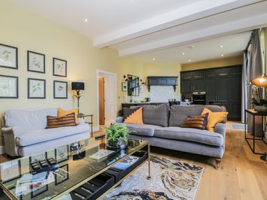 A living room with two sofas and a glass coffee table next to an open kitchen with dark cabinets at Tarn End Cottages 5 Talkin near Brampton Cumbria