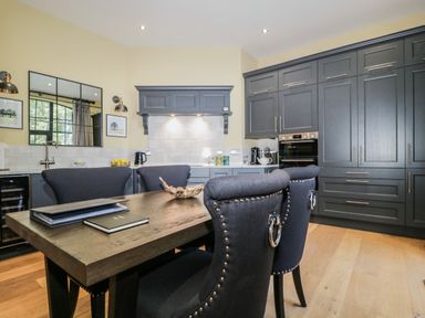 A kitchen with dark cabinets a wooden table with dark chairs and books on the table at Tarn End Cottages 5 Talkin near Brampton Cumbria