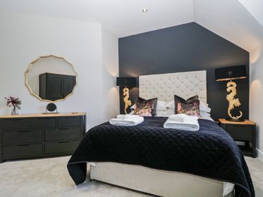A bedroom with a double bed with black bedding and white headboard black bedside tables with lamps and a black dresser with a mirror at Tarn End Cottages 5 Talkin near Brampton Cumbria