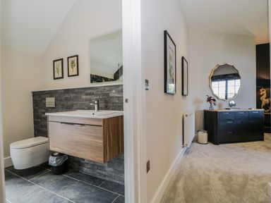A bathroom with a toilet and sink on the left and a room with a black dresser and mirror on the right at Tarn End Cottages 5 Talkin near Brampton Cumbria