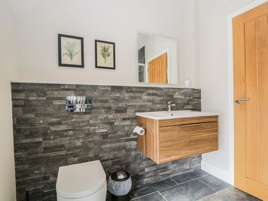 A bathroom with a wall-mounted wooden sink cabinet a white toilet and two framed plant pictures at Tarn End Cottages 5 Talkin near Brampton Cumbria