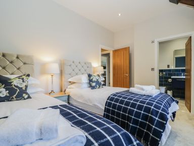A bedroom with two single beds each with a checkered blanket and folded towels between two wooden doors at Tarn End Cottages 5 Talkin near Brampton Cumbria