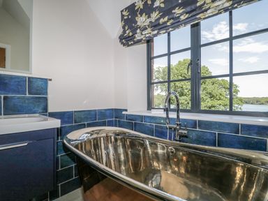 A bathroom with a metal bathtub and blue tiled walls near a window with a floral blind at Tarn End Cottages 5 Talkin near Brampton Cumbria