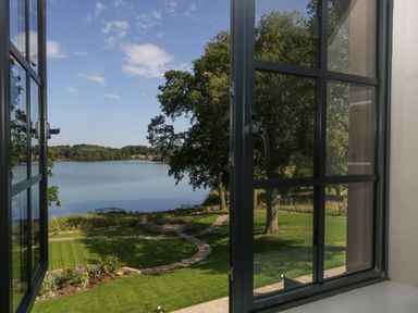 A view of a lake and trees from an open window with a garden and pathway outside at Tarn End Cottages 5 in Talkin near Brampton Cumbria
