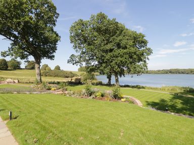 A garden with grass trees flowerbeds and a lake in the background at Tarn End Cottages 5 Talkin near Brampton Cumbria