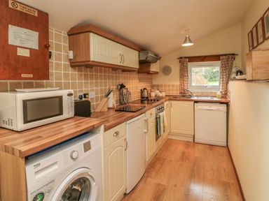A kitchen with a washing machine microwave stove dishwasher and a window with curtains at Beech Cottage in Combe Martin