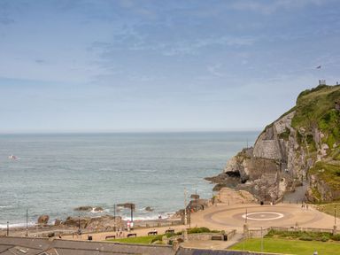 A coastal view with a rocky cliff a circular paved area benches and people by the sea at Beech Cottage in Combe Martin
