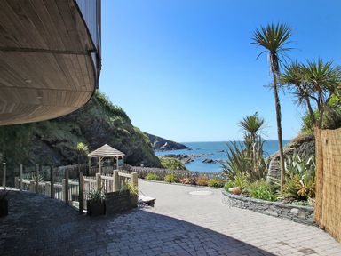 An outdoor area with stone pavement, plants, a wooden gazebo, cliffs, and a view of the sea at Beech Cottage in Combe Martin