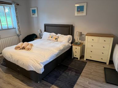 A bedroom with a bed with white bedding towels on the bed nightstands with lamps a dresser and a window at Beech Cottage in Combe Martin