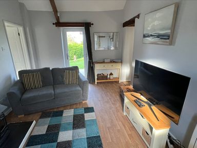 A living room with a grey sofa and striped cushions a TV on a stand a patterned rug and a console table with a mirror at Beech Cottage in Combe Martin