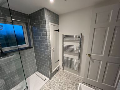 A bathroom with a shower enclosure tiled in gray subway tiles and a patterned floor at Beech Cottage in Combe Martin