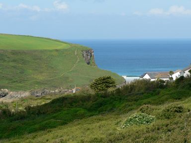 A coastal landscape with green hills white houses and the ocean in the background at Porth Farm Annexe in Mawgan Porth