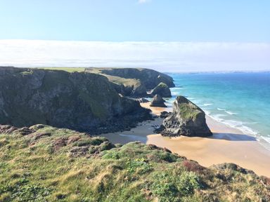A coastal cliff with rocky formations and a sandy beach by the sea at Porth Farm Annexe in Mawgan Porth