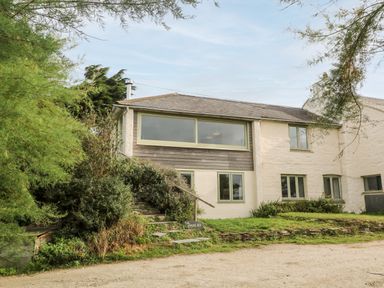 A building with multiple windows surrounded by trees and shrubs at Porth Farm Annexe in Mawgan Porth
