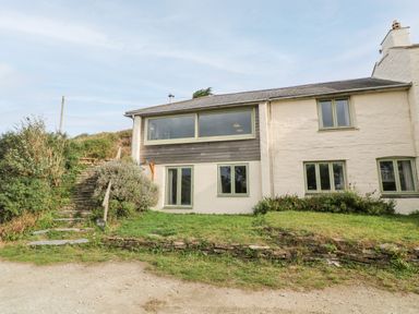 Exterior view of a two-story house with stone steps and greenery at Porth Farm Annexe in Mawgan Porth