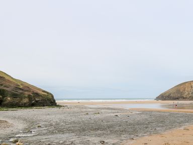 A sandy beach with cliffs on both sides and a few people walking near the shoreline at Porth Farm Annexe in Mawgan Porth
