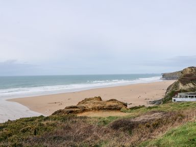A sandy beach with ocean waves and rocky cliffs with some vegetation at Porth Farm Annexe in Mawgan Porth