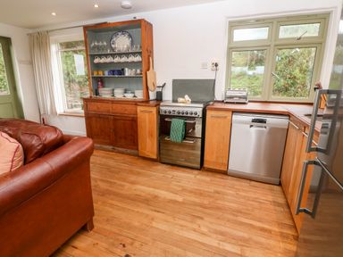 A kitchen with wooden cabinets a stove dishwasher and a wooden cupboard displaying dishes at Porth Farm Annexe Mawgan Porth