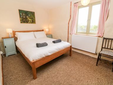 A bedroom with a wooden double bed two bedside tables with lamps a window with striped curtains and a wooden chair at Porth Farm Annexe in Mawgan Porth