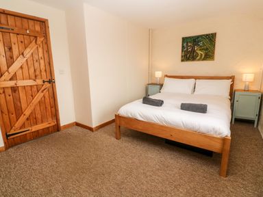 A bedroom with a wooden bed frame white bedding two gray towels two bedside tables with lamps and a wooden door at Porth Farm Annexe in Mawgan Porth
