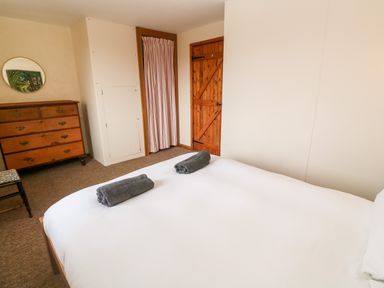 A bedroom with a double bed with white sheets and two rolled towels a wooden dresser a chair a wooden door and a small closet at Porth Farm Annexe in Mawgan Porth