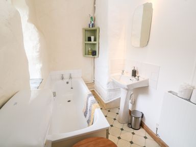 A bathroom with a bathtub a pedestal sink a mirror and a small green shelf on the wall at Porth Farm Annexe in Mawgan Porth