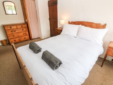 A bedroom with a double bed with two rolled towels on it a wooden dresser with a mirror a bedside table with a lamp and a wooden door at Porth Farm Annexe Mawgan Porth
