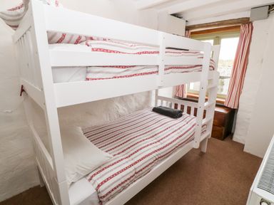 A small bedroom with a white bunk bed and red and white striped bedding at Porth Farm Annexe in Mawgan Porth