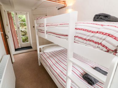 A bedroom with a white bunk bed and striped bedding next to a door with glass panels at Porth Farm Annexe in Mawgan Porth