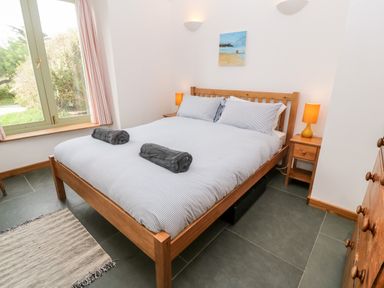 A bedroom with a wooden double bed two bedside tables with orange lamps a window and a chest of drawers at Porth Farm Annexe in Mawgan Porth