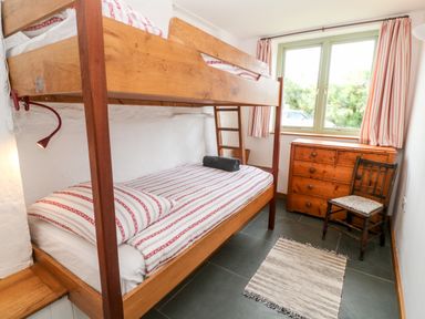 A bedroom with wooden bunk beds a wooden chest of drawers a wooden chair and a small rug on the floor at Porth Farm Annexe in Mawgan Porth