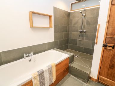 A bathroom with a bathtub with a towel and a shower area with grey tiles at Porth Farm Annexe in Mawgan Porth