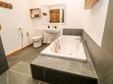 A bathroom with a bathtub sink toilet mirror and wooden door at Porth Farm Annexe in Mawgan Porth