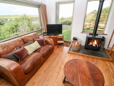 A living room with a brown leather sofa a television a wood stove and a wooden coffee table at Porth Farm Annexe in Mawgan Porth