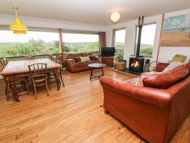A living room with brown leather sofas a wooden dining table and chairs a fireplace and a television at Porth Farm Annexe Mawgan Porth
