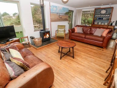 A living room with two leather sofas a wood burning stove a round wooden coffee table and a cabinet with dishes at Porth Farm Annexe Mawgan Porth