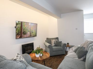 A living room with grey sofas a wooden coffee table a wall-mounted tv and plants at Y Goedwig in Newborough