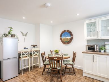 A kitchen with a refrigerator table and chairs microwave and wall clock at Y Goedwig in Newborough