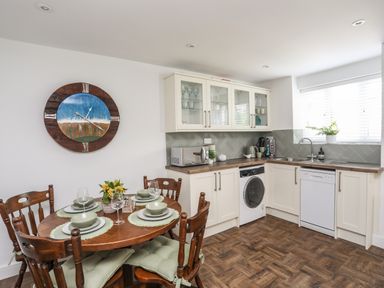 A kitchen with wooden dining table set with plates and glasses next to white cabinets and a washing machine at Y Goedwig in Newborough