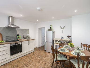 A kitchen with white cabinets a dining table set for four and a refrigerator at Y Goedwig in Newborough