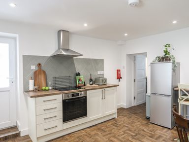 A kitchen with white cabinets a stainless steel oven and fridge a wooden countertop and a tiled backsplash at Y Goedwig in Newborough