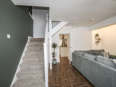 A living room with a gray sofa a carpeted staircase and a view into the kitchen at Y Goedwig in Newborough